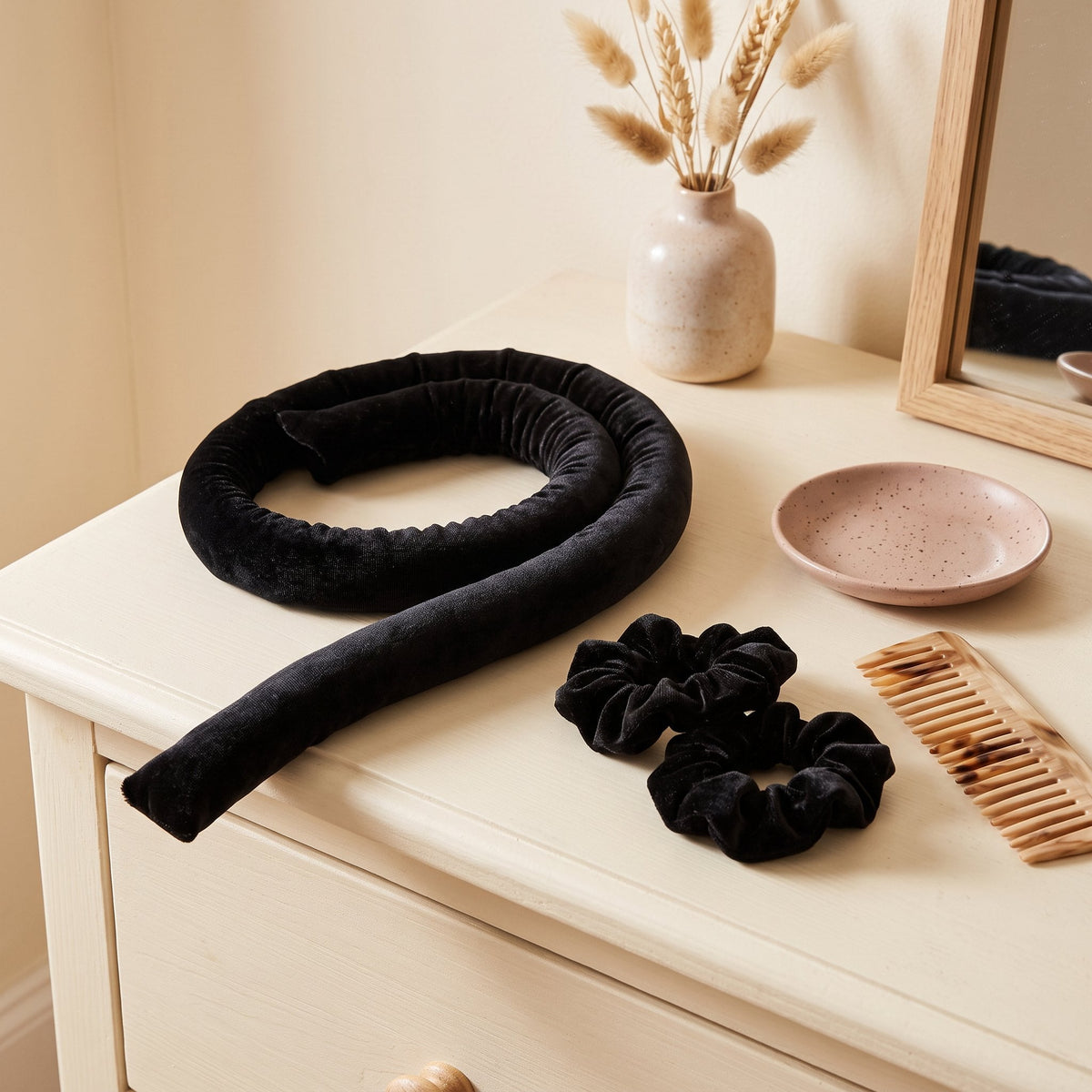 Black velvet heatless curling rod coiled with two scrunchies on a dresser