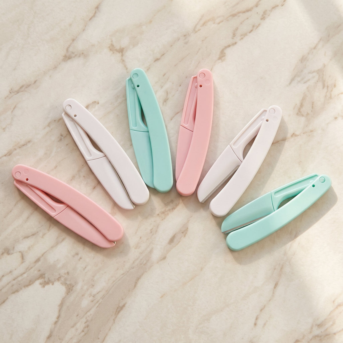 Six folding face razors in pink, white and mint fanned on marble